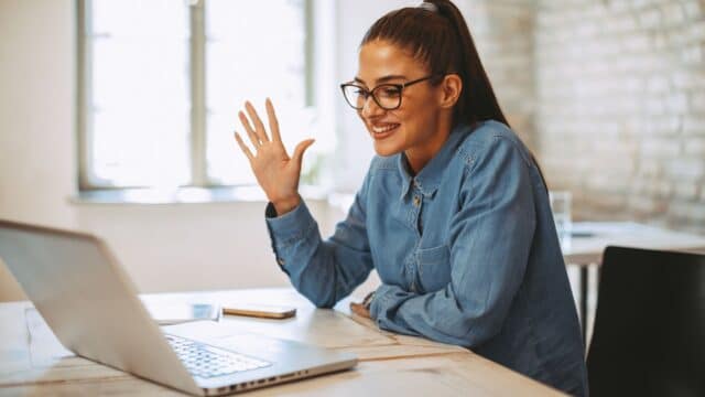 Trendy office worker at computer holding up her hand