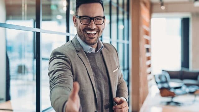 Professional man in office extends hand while smiling