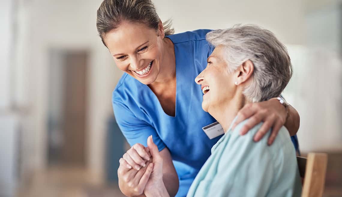 Smiling caregiver supporting sitting patient and holding her hand