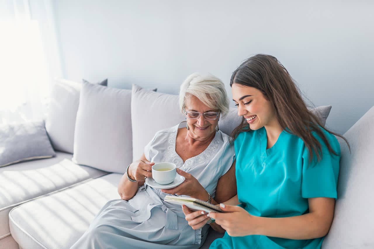 Caregiver and patient sitting on a couch both smiling looking at caregiver's notes