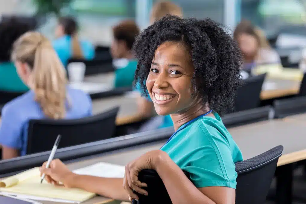 woman in a classroom sitting and writing looking back and smiling