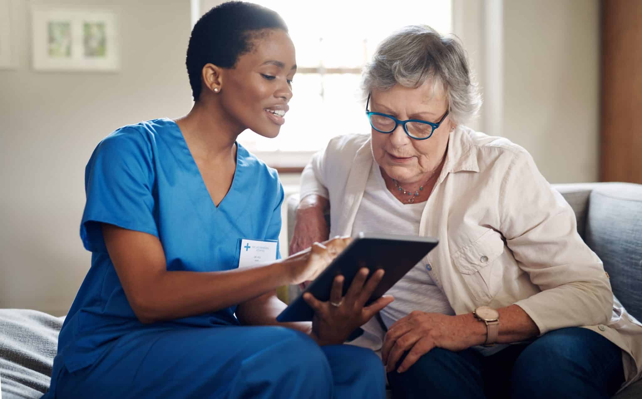 Shot of a senior woman using a digital tablet with a nurse on the sofa at home